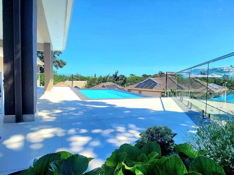 Spacious covered patio featuring a modern swimming pool and glass balustrade, offering an elevated outdoor entertainment area with scenic views.