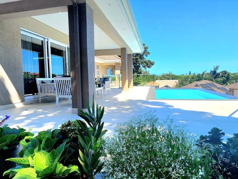 Spacious covered patio overlooking a swimming pool with modern glass balustrades and tiled flooring, offering a seamless indoor-outdoor living experience.