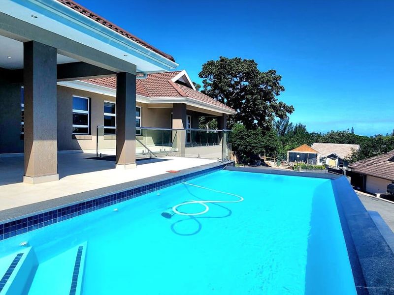 An elevated infinity edge swimming pool overlooking the property grounds, featuring a spacious tiled patio area with glass balustrades and modern architectural finishes.