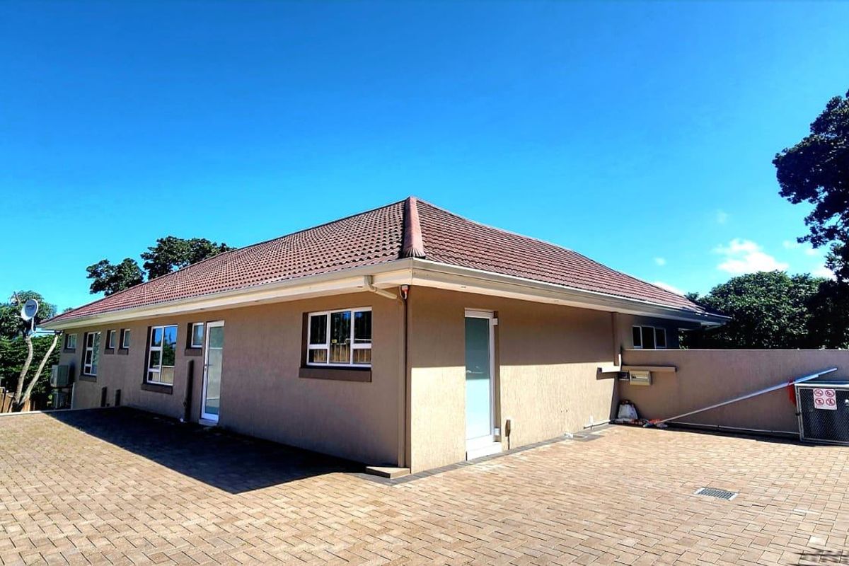 Rear exterior view of the house featuring a paved courtyard, tiled roof, and surrounding retaining walls.