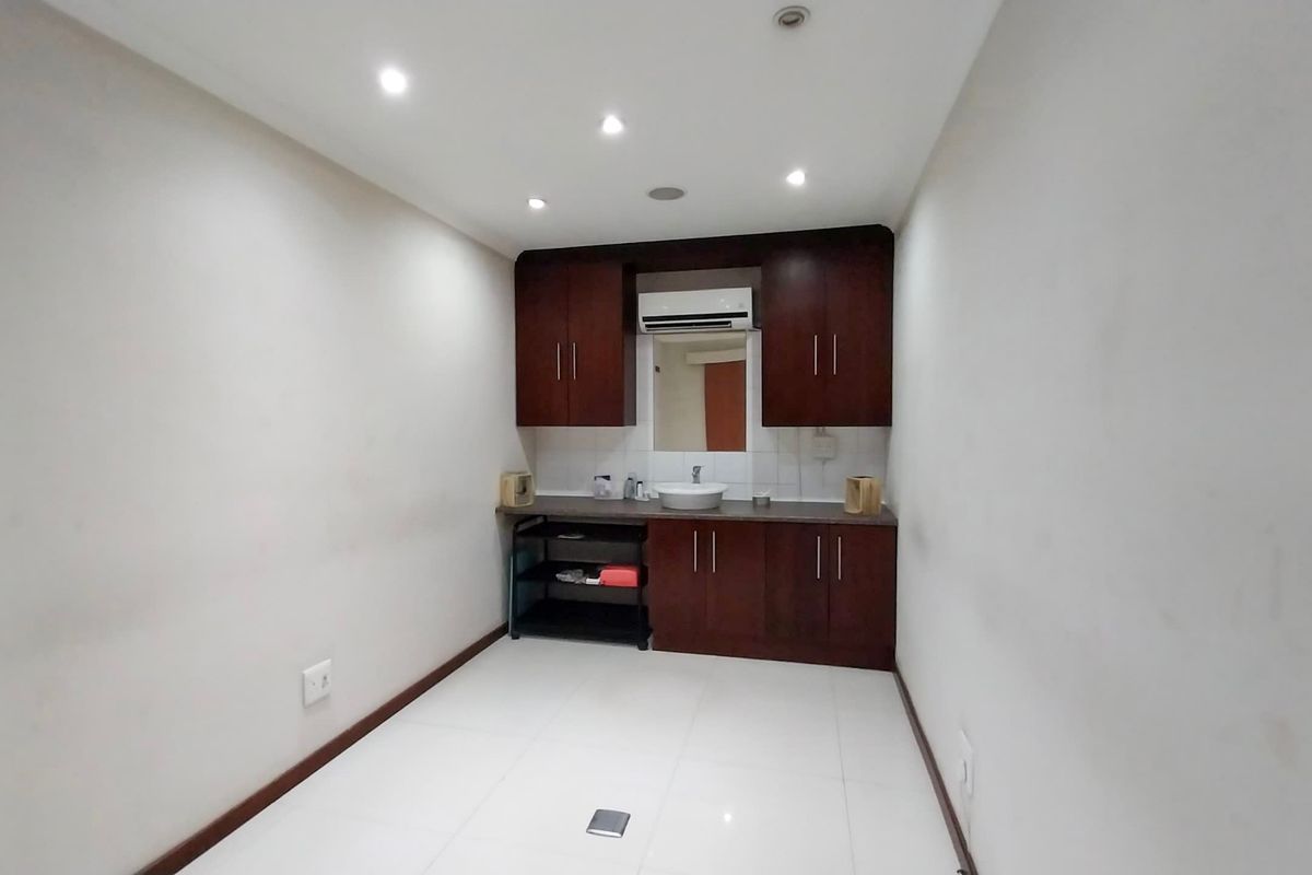 A compact kitchenette featuring dark wood cabinetry, a basin, and tiled flooring, suitable for a small office or commercial utility space.