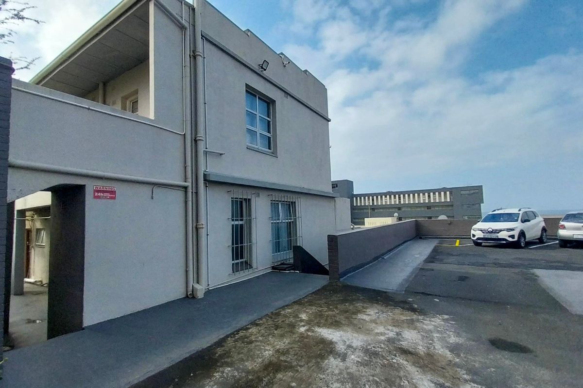 Rear exterior view of the commercial building featuring an asphalt parking area, security-fitted windows, and concrete retaining walls.