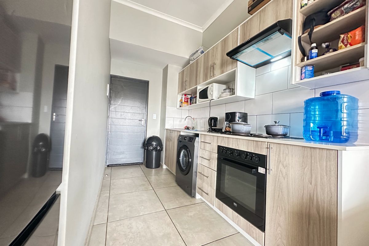 A compact, modern kitchen featuring light wood-grain cabinetry, built-in oven, hob, extractor fan, and integrated laundry plumbing.
