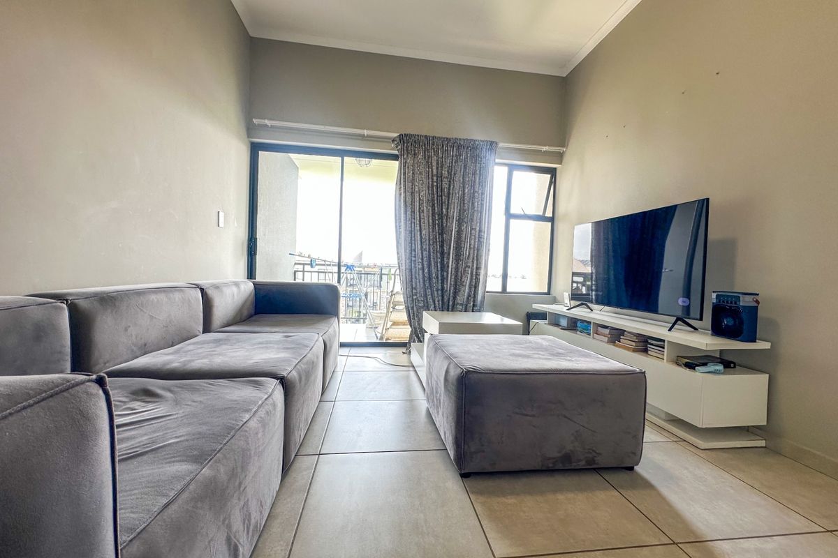A comfortable living room featuring large format floor tiles, sliding glass doors leading to a balcony, and neutral wall finishes.