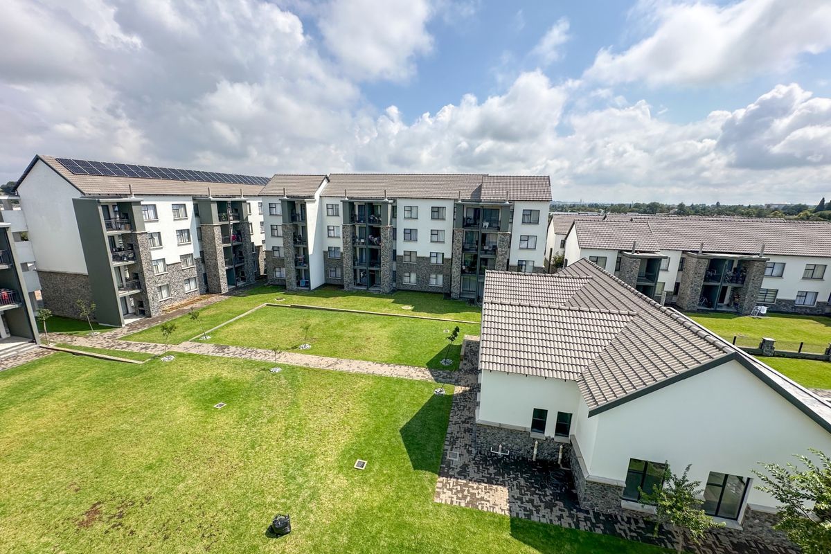 An elevated aerial view of a modern apartment complex featuring multiple residential blocks, tiled roofs, solar panels, and well-maintained communal garden areas.