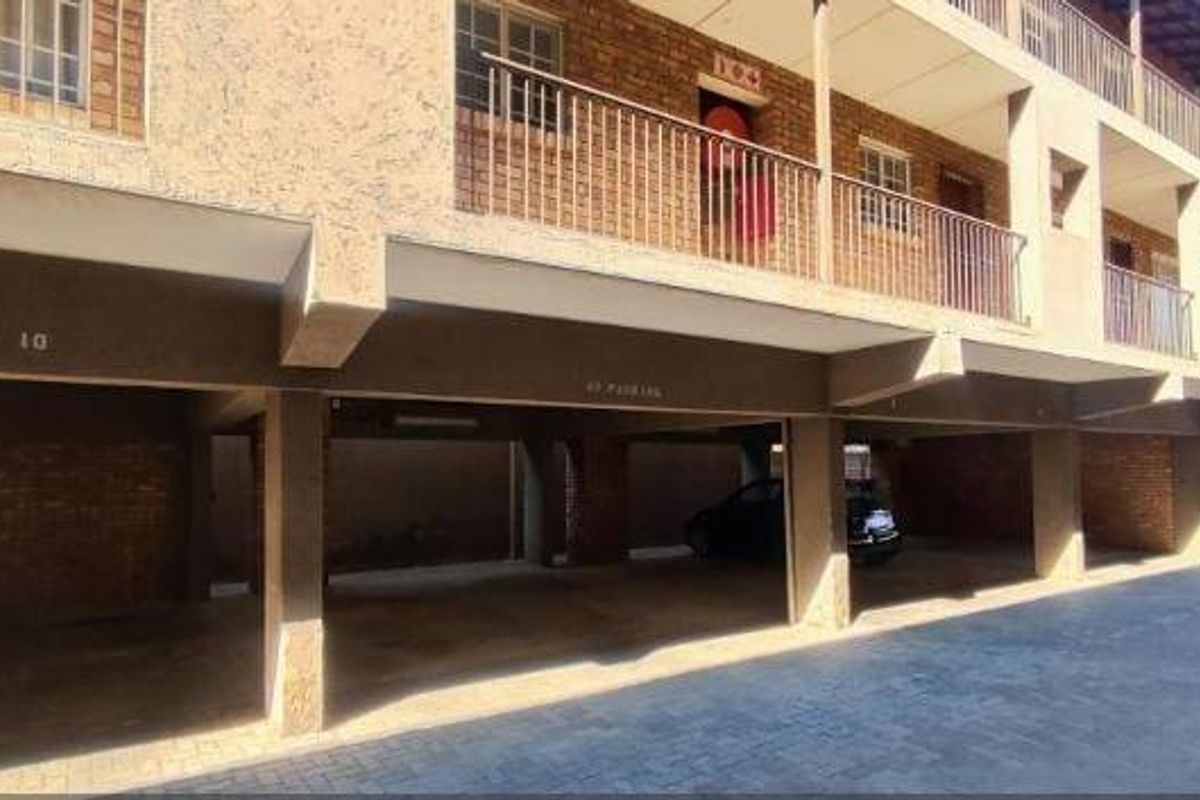 A view of the apartment building's ground-level covered parking area with brick facade and upper-level balconies.