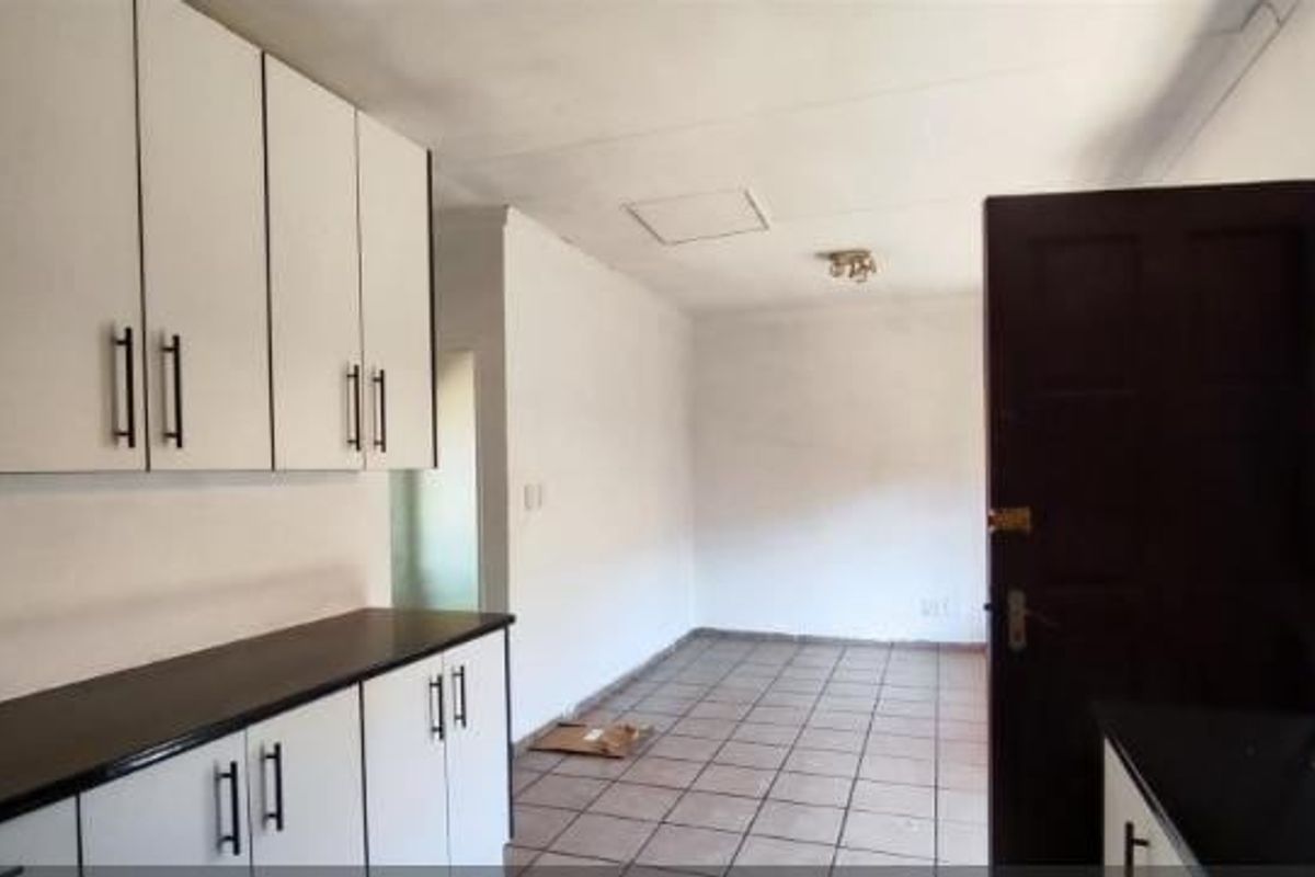 A functional kitchen area featuring white built-in cabinetry, dark countertops, and tiled flooring, presenting a clean, empty space ready for personalization.