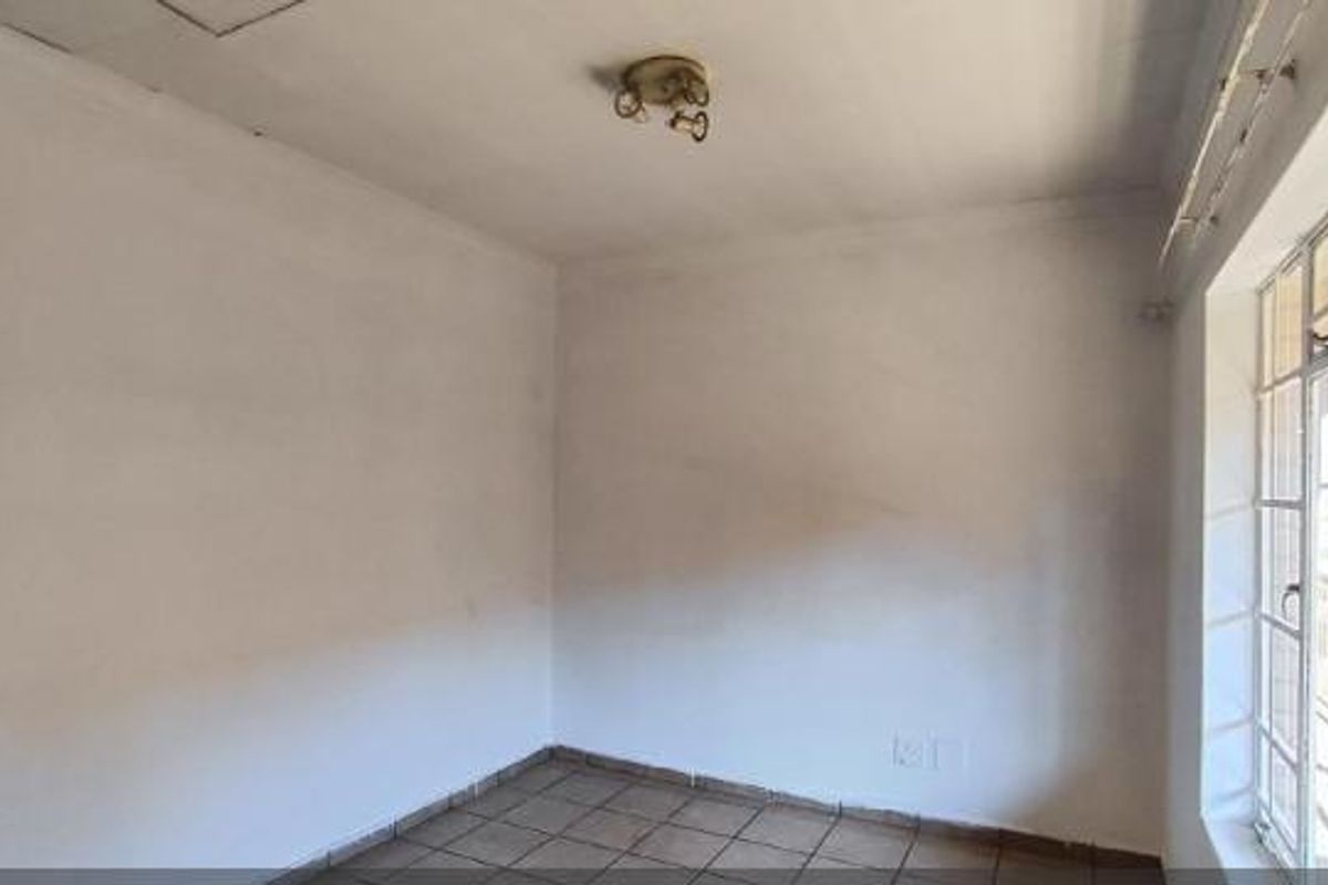 An empty bedroom featuring tiled flooring, a steel-framed window, and a ceiling-mounted light fixture, ready for personalization.