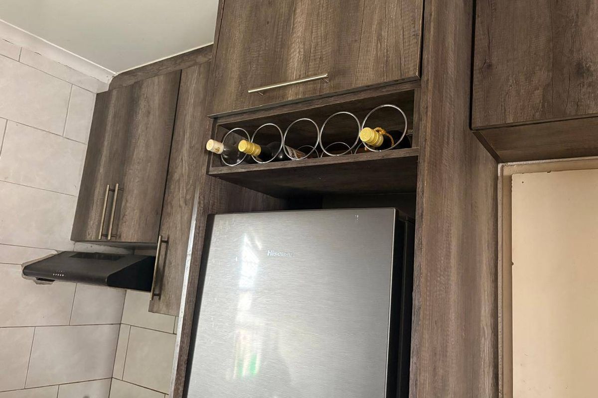 A kitchen section featuring dark wood-grain cabinetry, a built-in wine rack, and a tiled splashback with an integrated extractor fan.