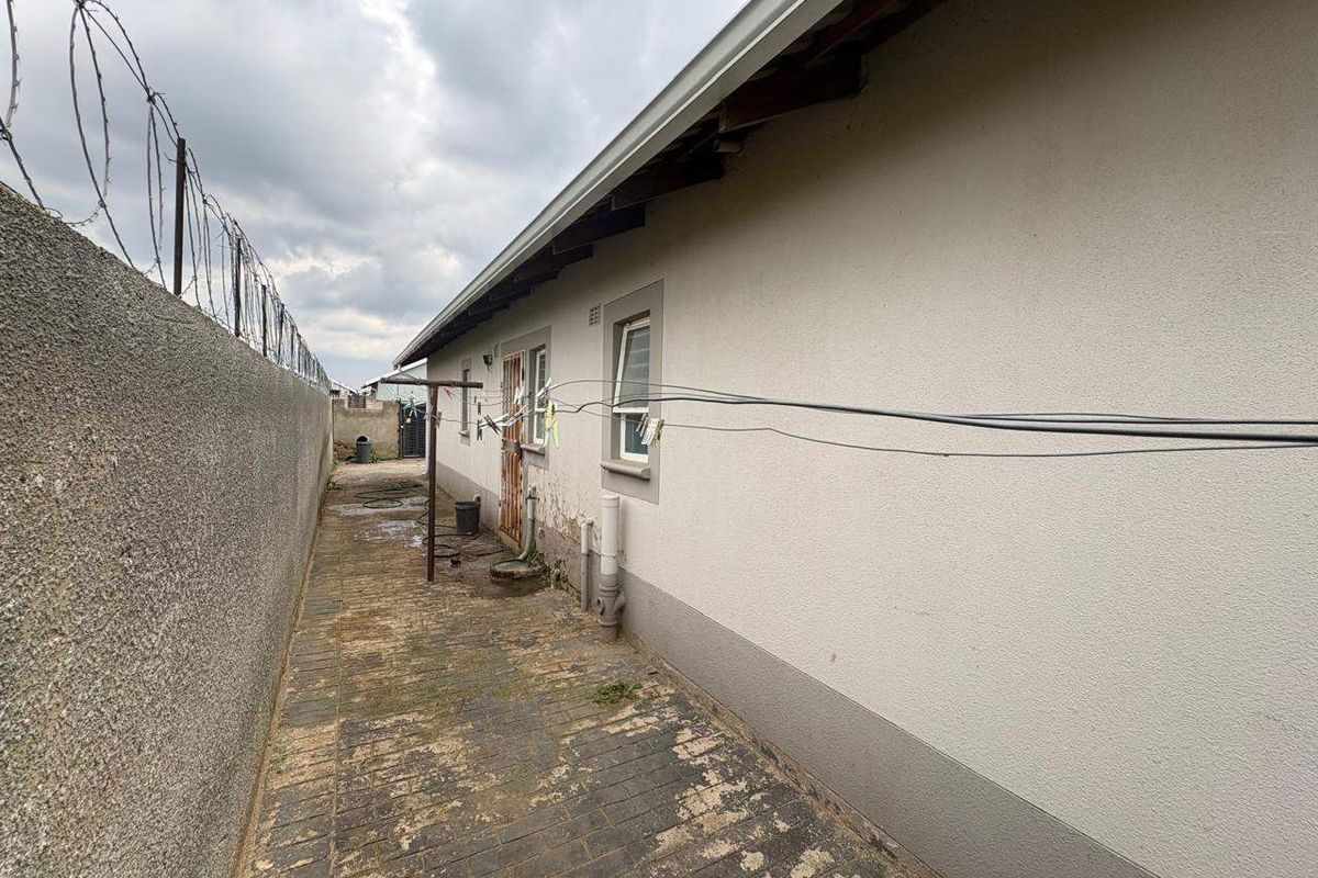 Side exterior view of the property featuring a paved walkway, security wall with razor wire, and external plumbing fixtures.
