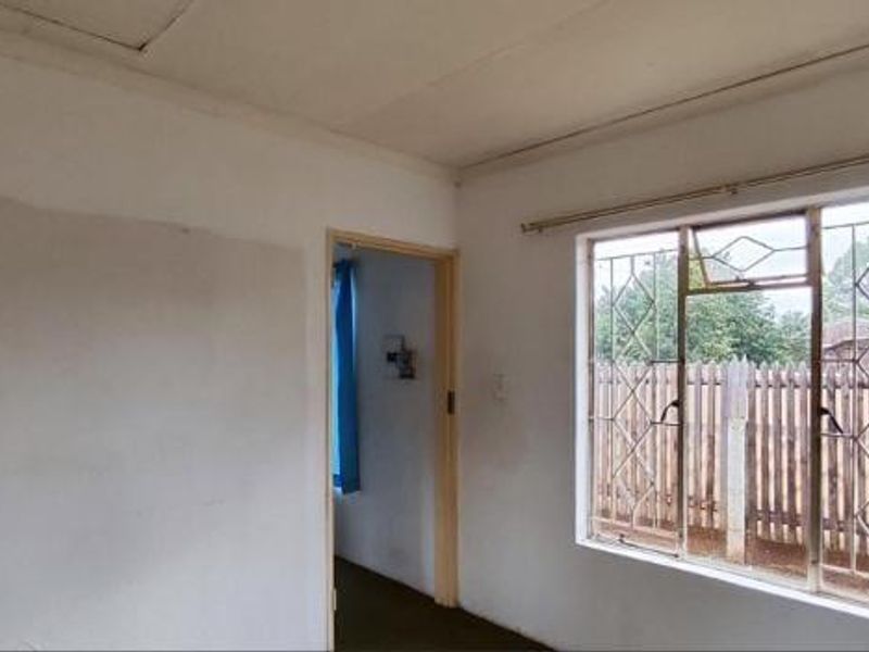 An empty bedroom featuring a window with security bars and a curtain rail, requiring cosmetic updates to the walls and ceiling.