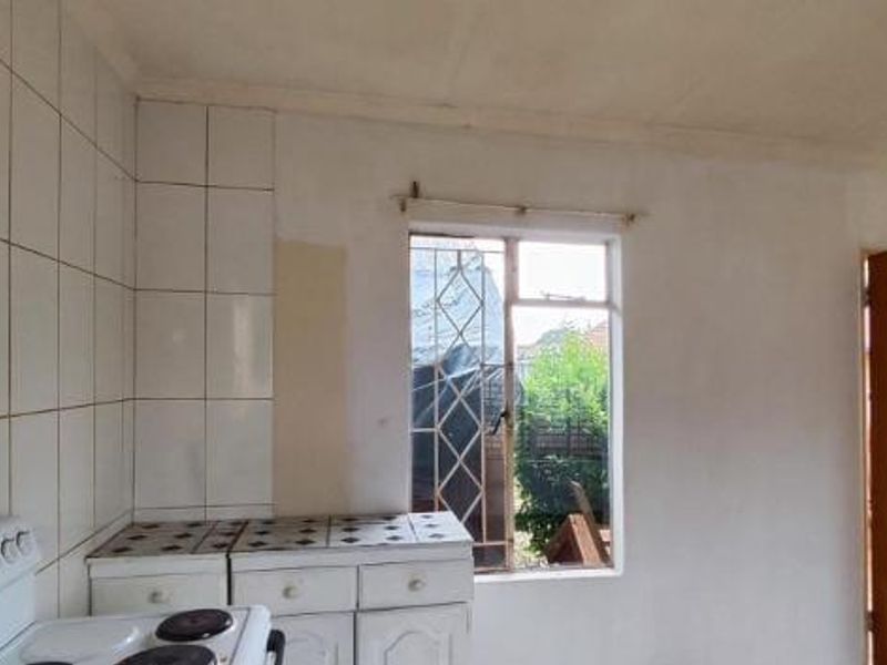 A basic kitchen area featuring tiled splashbacks, built-in cabinetry with tiled countertops, and a freestanding stove, awaiting modernization.
