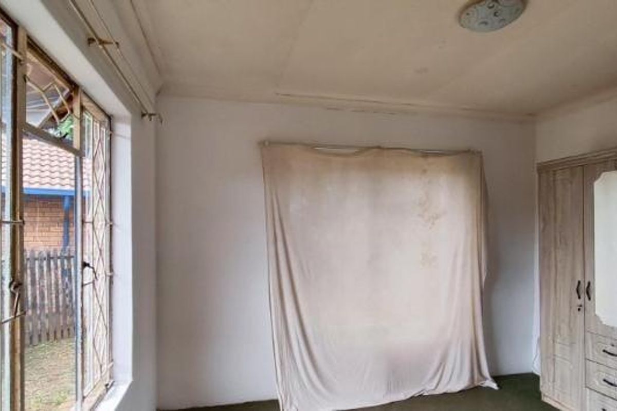 A bedroom featuring a built-in wardrobe, security bars on the windows, and a ceiling light fixture, requiring cosmetic updates to improve its condition.