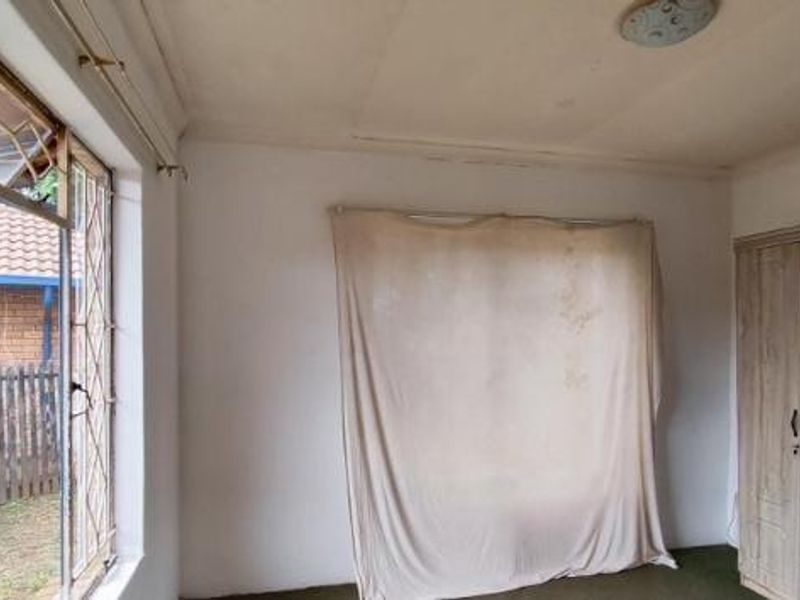 A bedroom featuring a built-in wardrobe, security bars on the windows, and a ceiling light fixture, requiring cosmetic updates to improve its condition.