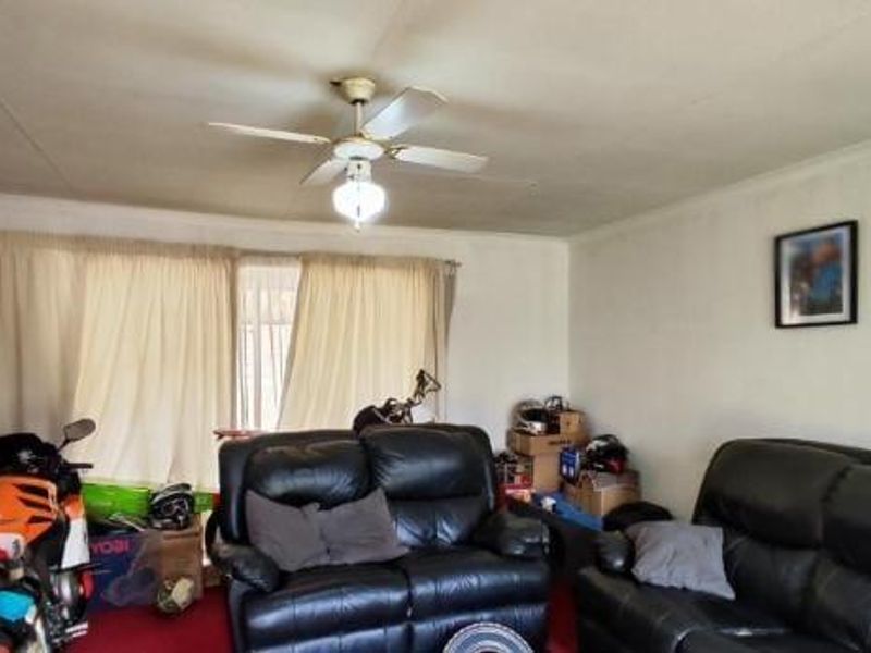 A living room space featuring a ceiling fan and large window with curtain tracks, requiring cosmetic updates to improve the overall finish.