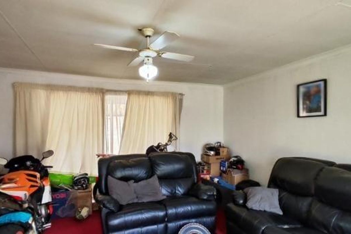 A living room space featuring a ceiling fan and large window with curtain tracks, requiring cosmetic updates to improve the overall finish.