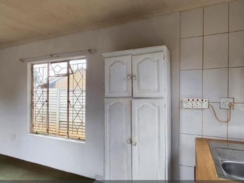 A functional kitchen area featuring a stainless steel sink, tiled splashback, and built-in pantry storage, requiring cosmetic updates to modernize the space.