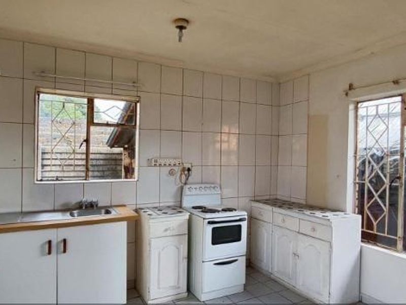 A dated kitchen featuring white cabinetry, tiled walls, a stainless steel sink, and a freestanding stove, offering potential for a modern renovation.