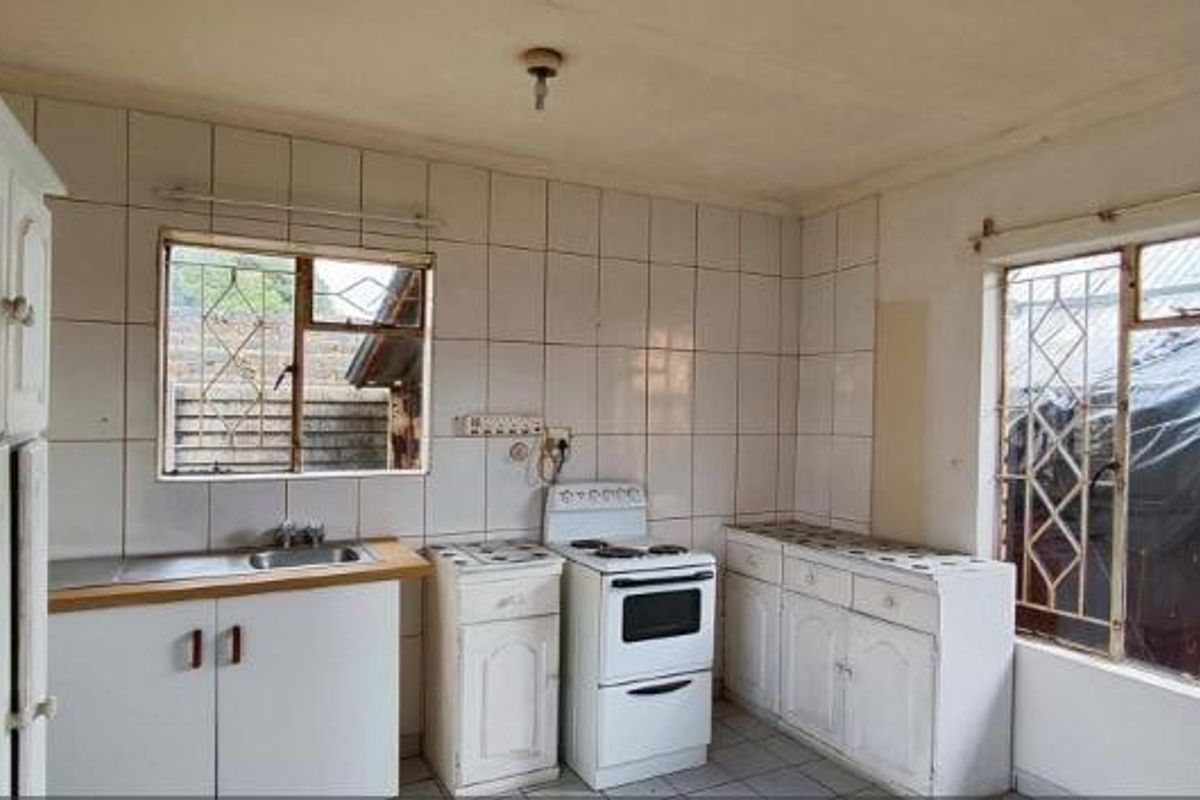 A dated kitchen featuring white cabinetry, tiled walls, a stainless steel sink, and a freestanding stove, offering potential for a modern renovation.