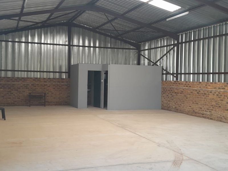 Spacious industrial utility area featuring concrete flooring, exposed steel roof structure, face brick walls, and a central enclosed office partition.