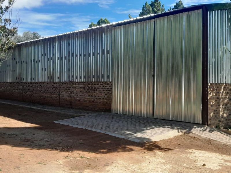 Rear view of an industrial structure featuring corrugated metal cladding, a brick base, and large sliding access doors with paved exterior pathways.