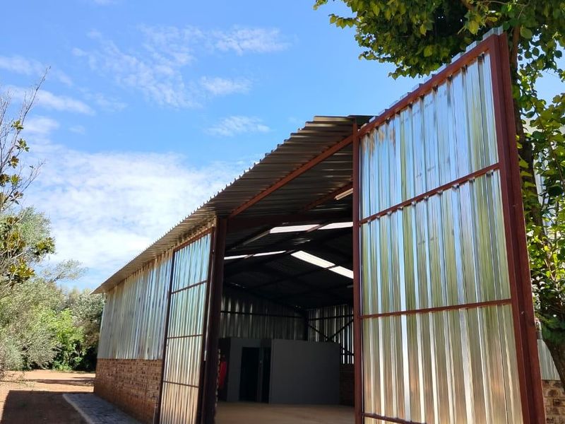 Spacious industrial-style warehouse or garage featuring a steel frame, corrugated metal walls, large sliding doors, and concrete flooring with natural overhead lighting.
