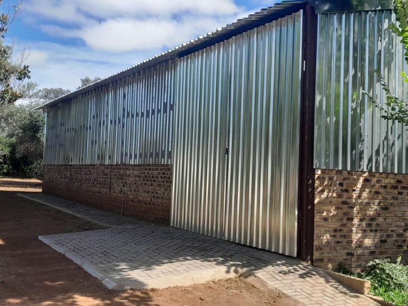 Rear view of an industrial-style building featuring corrugated metal cladding, a face brick base, and a paved access path.