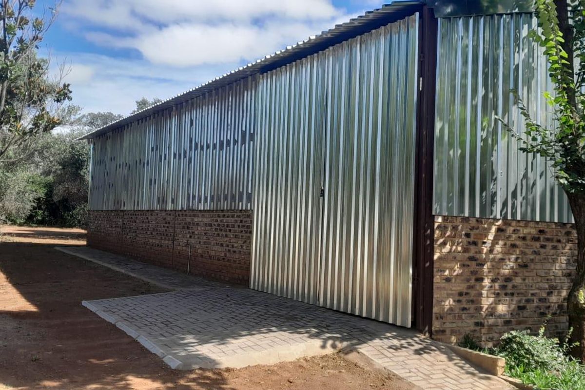 Rear view of an industrial-style building featuring corrugated metal cladding, a face brick base, and a paved access path.