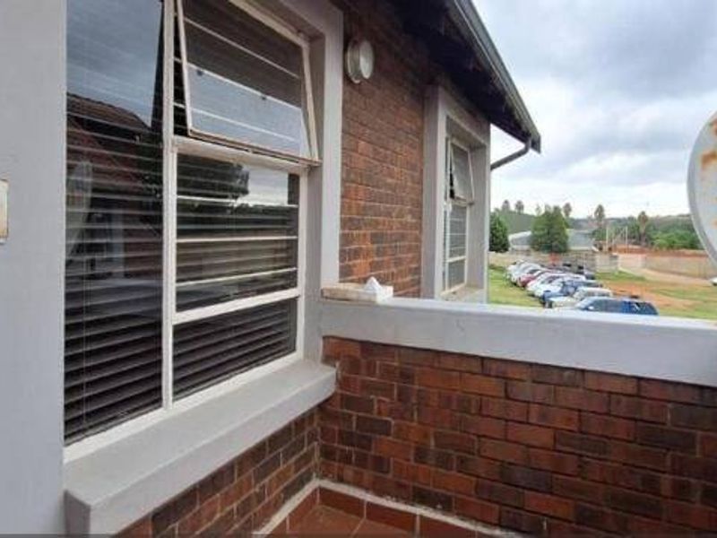 A compact balcony featuring exposed brick walls, tiled flooring, and a satellite dish, offering an elevated view of the surrounding parking area.