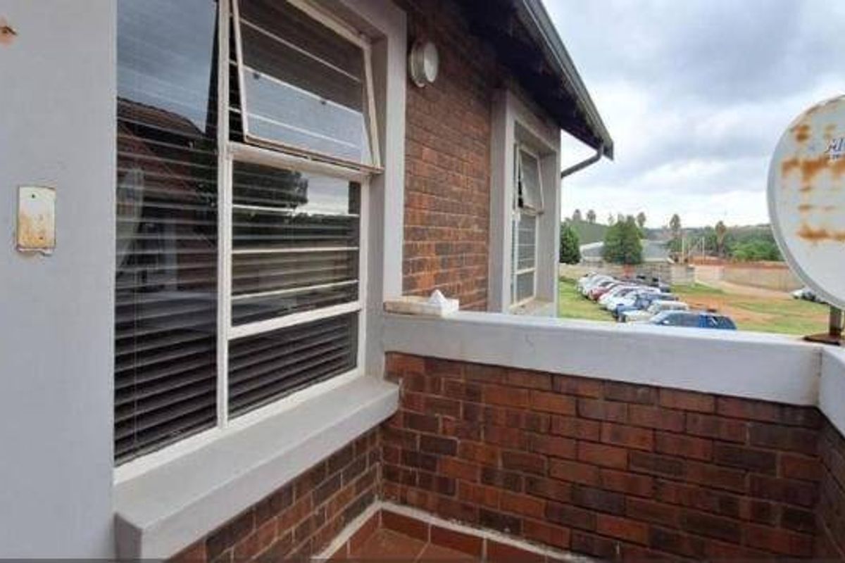A compact balcony featuring exposed brick walls, tiled flooring, and a satellite dish, offering an elevated view of the surrounding parking area.
