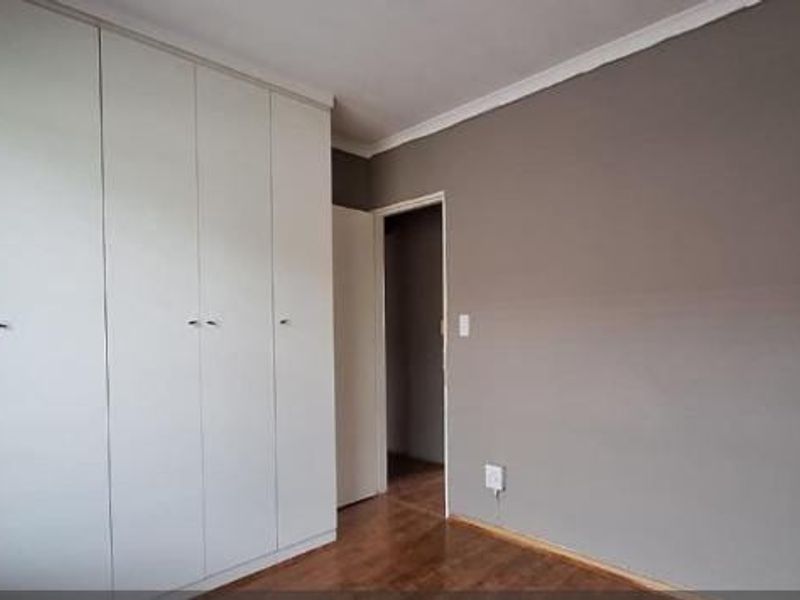 A clean, empty bedroom featuring neutral grey walls, laminate flooring, and ample built-in cupboard storage.