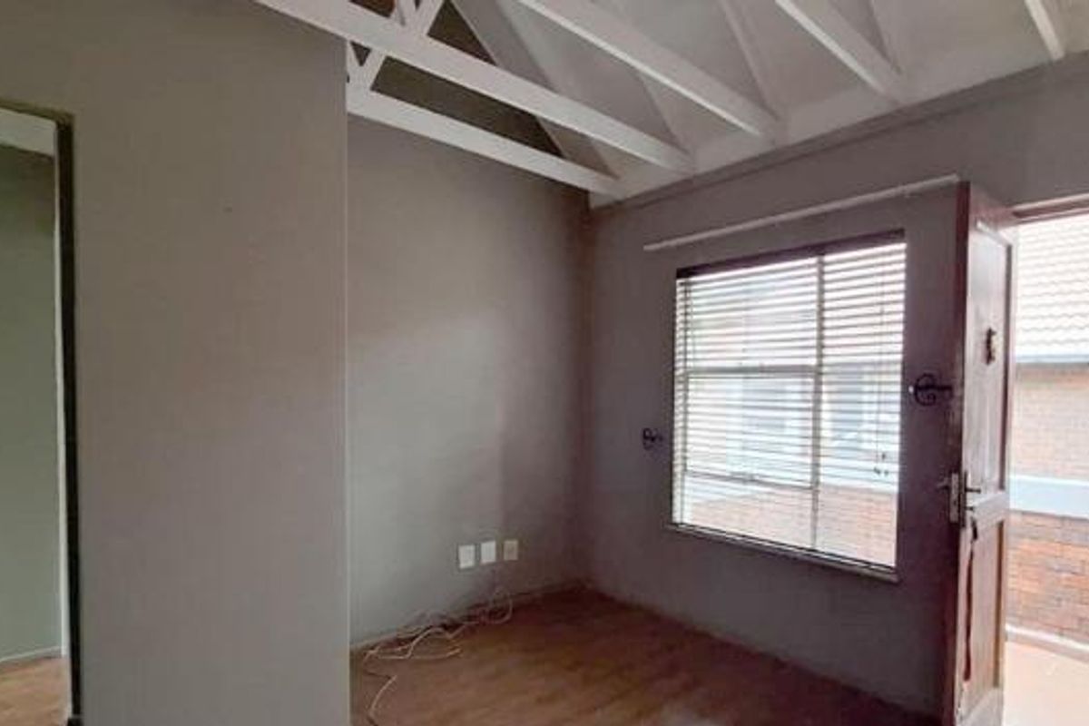 An empty bedroom featuring exposed white timber rafters, laminate flooring, and a door leading to an exterior balcony with a security gate.
