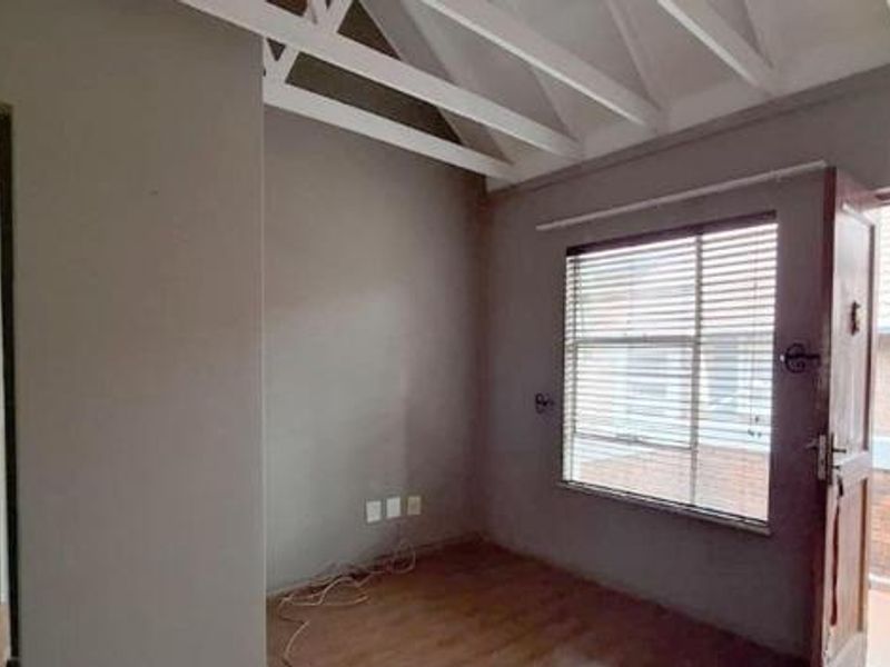 An empty bedroom featuring exposed white timber rafters, laminate flooring, and a door leading to an exterior balcony with a security gate.