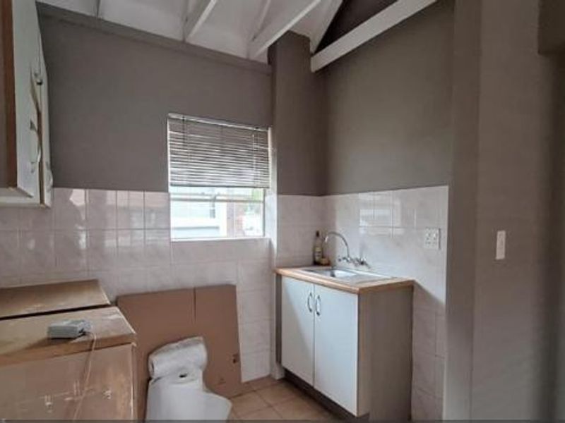 A compact kitchen area featuring basic cabinetry, a stainless steel sink, tiled backsplash, and exposed ceiling rafters, offering potential for modernization.