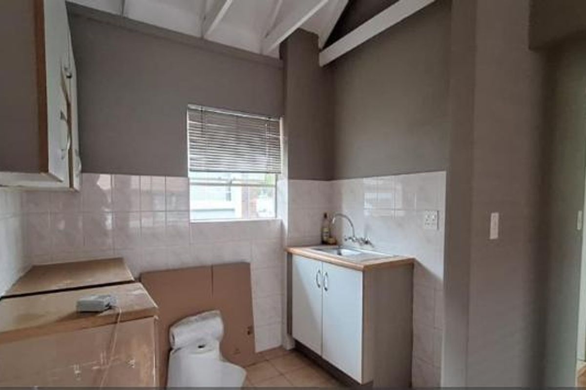 A compact kitchen area featuring basic cabinetry, a stainless steel sink, tiled backsplash, and exposed ceiling rafters, offering potential for modernization.