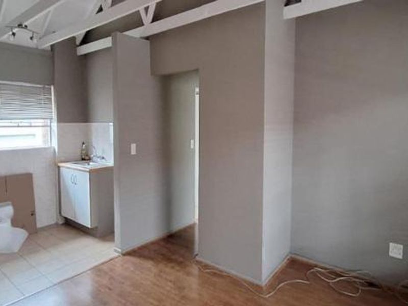 Open plan living area featuring exposed roof trusses, laminate flooring, and a partially finished kitchen area with built-in cabinetry and sink.