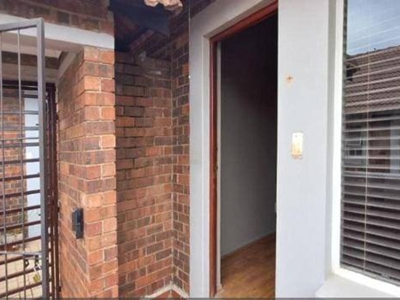 Entrance area featuring a security gate, brick exterior wall, and access to the interior with laminate flooring visible through the doorway.