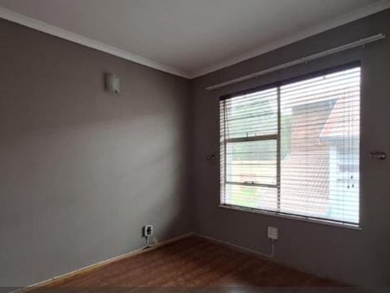 A bright, empty bedroom featuring laminate flooring, a built-in cupboard, and large windows fitted with venetian blinds.