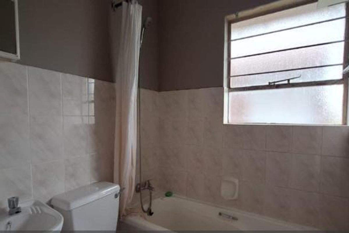 A functional bathroom featuring a bathtub with shower attachment, pedestal basin, and toilet, finished with neutral wall tiling and a window for natural light.
