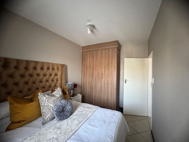 A well-maintained bedroom featuring neutral wall tones, tiled flooring, and a functional built-in wooden wardrobe.