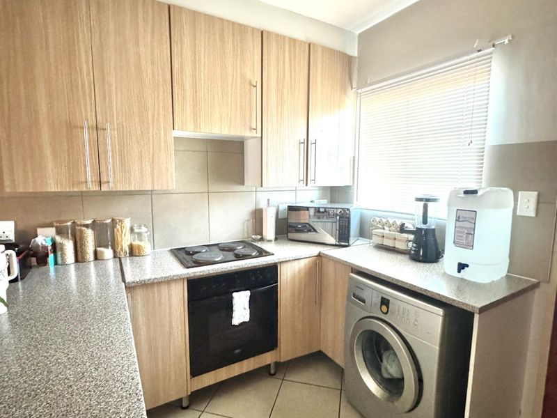 A functional kitchen featuring light wood-finish cabinetry, granite-look countertops, built-in oven and hob, and tiled flooring with a window for natural light.
