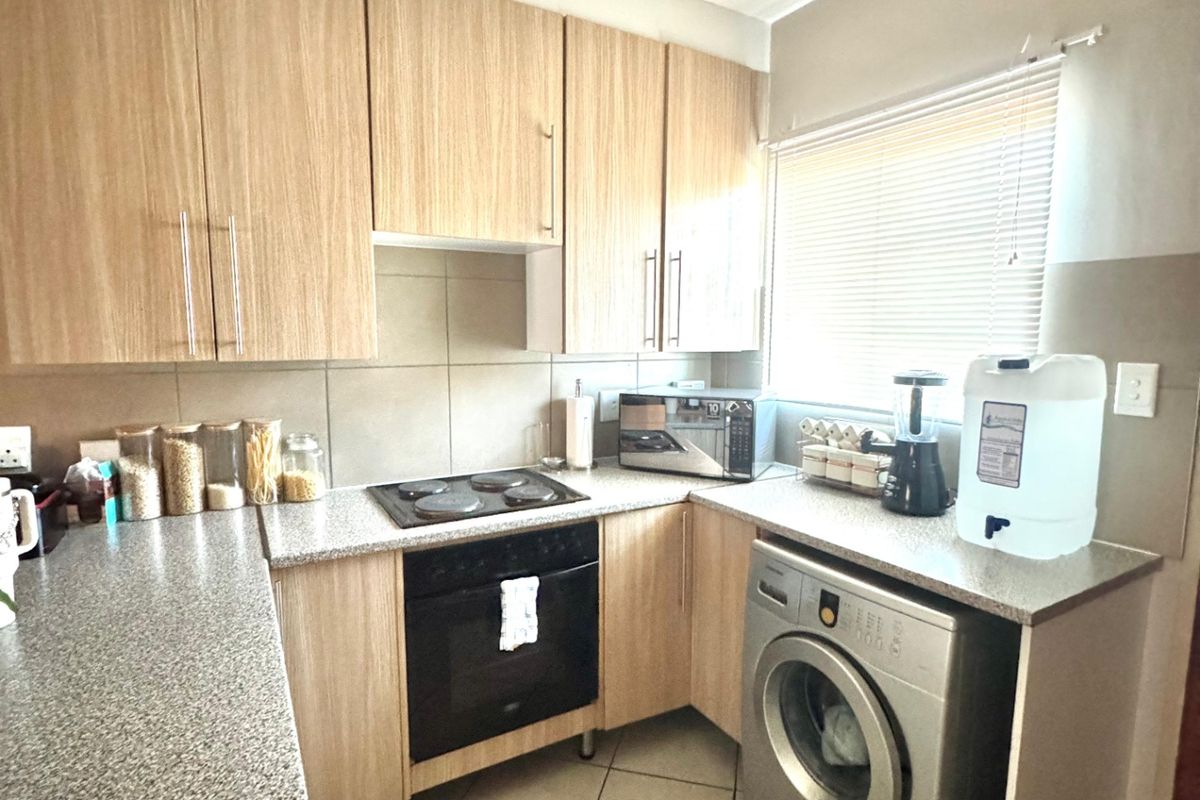 A functional kitchen featuring light wood-finish cabinetry, granite-look countertops, built-in oven and hob, and tiled flooring with a window for natural light.