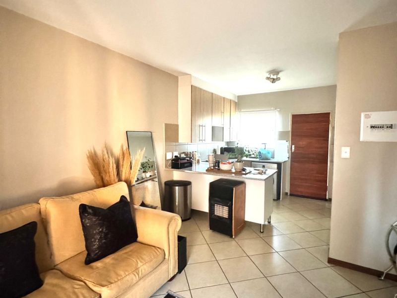 Open-plan living area featuring tiled flooring and a functional kitchen with built-in cabinetry, seamlessly connecting to the main entrance.
