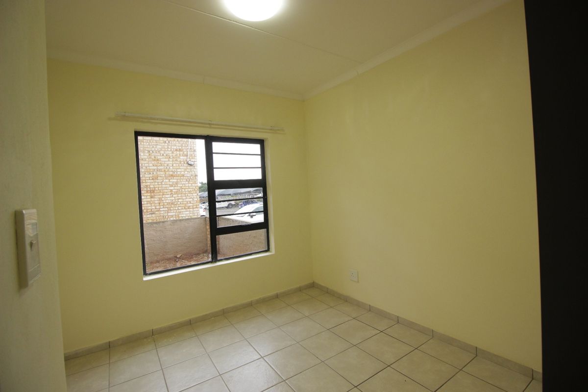 A clean, empty bedroom featuring neutral tiled flooring, a coved ceiling, and an aluminium-framed window providing natural light.