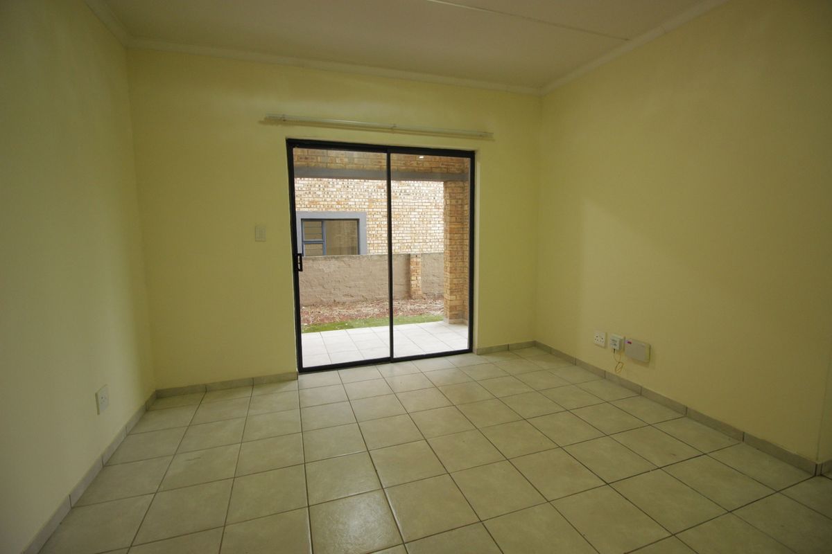 An empty living room featuring neutral tiled flooring and a sliding glass door providing access to an outdoor patio area.