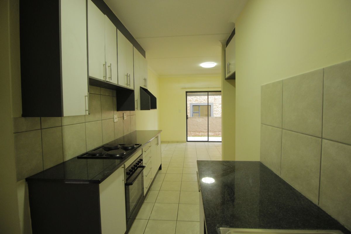 A clean, empty kitchen featuring modern built-in cabinetry, granite countertops, an integrated electric hob and oven, and tiled flooring leading to a sliding glass door.