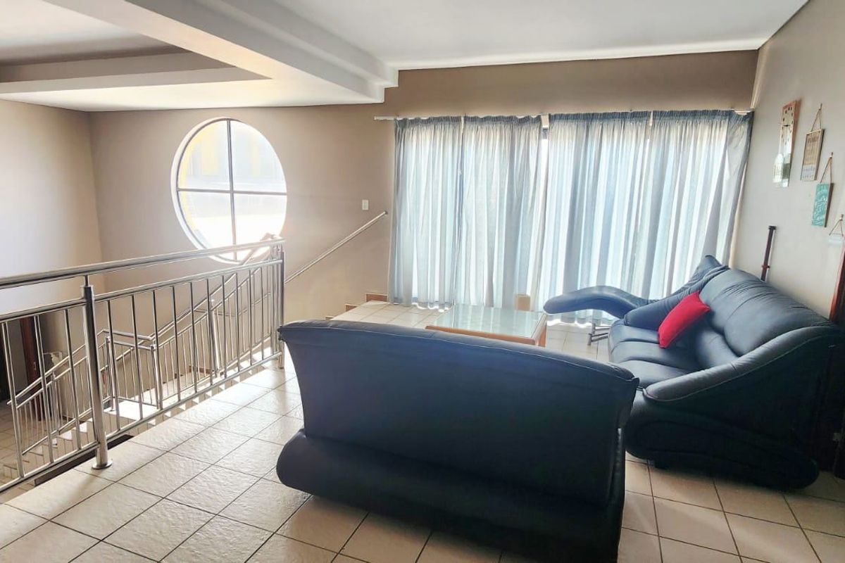 Spacious living area featuring tiled flooring, a modern stainless steel balustrade overlooking the lower level, and a distinctive circular window.
