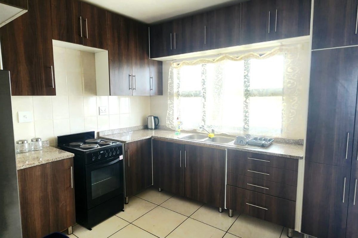 Functional kitchen featuring dark wood-look cabinetry, granite countertops, a double bowl sink, and a freestanding stove with tiled flooring and backsplash.