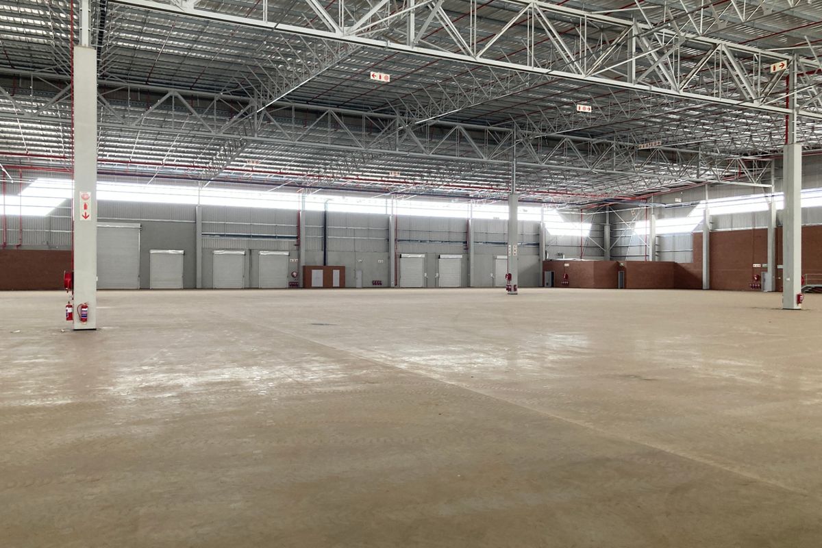 Expansive industrial warehouse space featuring high-clearance steel truss roofing, multiple roller shutter doors, and durable concrete flooring, suitable for logistics or manufacturing operations.