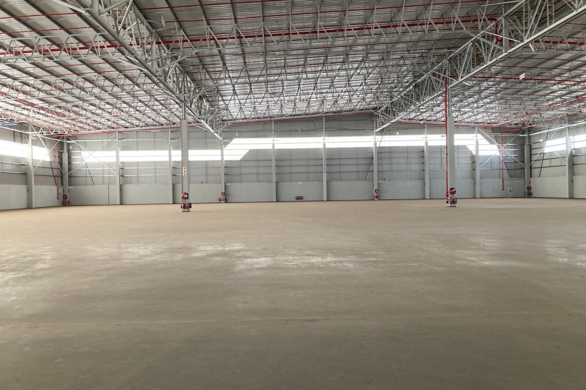 Expansive industrial warehouse space featuring high ceilings with exposed steel trusses, fire sprinkler system, and polished concrete flooring.